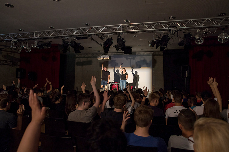 In einem abgedunkelten Saal heben Menschen im Publikum und die Redner eine Hand in die Höhe